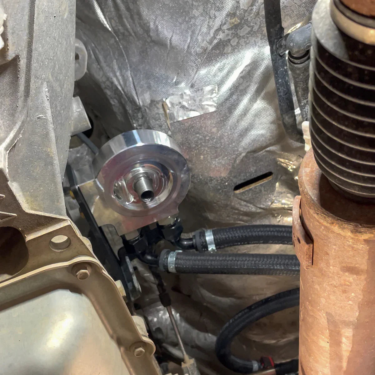 Underbody view of H&S Motorsports billet fuel filter relocation base installed on 2017–2023 Ford 6.7L Power Stroke, showing dual braided hoses connected.