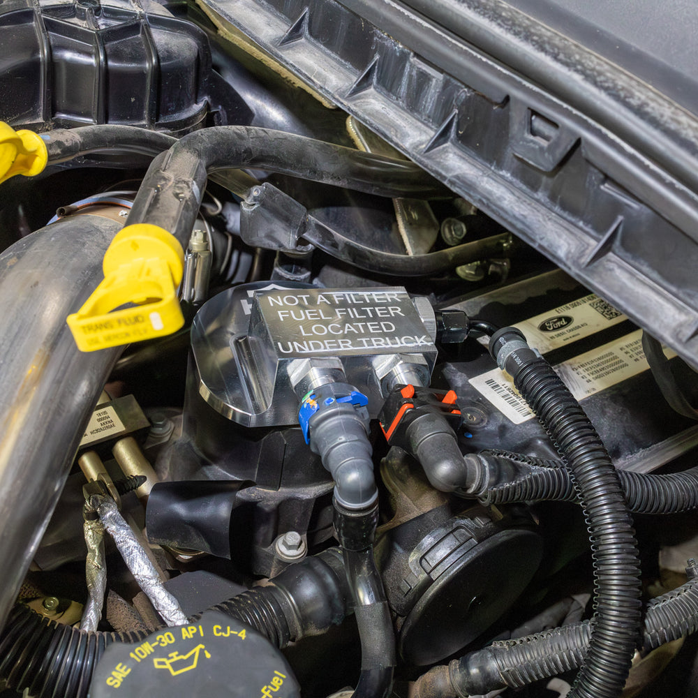 
                  
                    Installed view of HSM fuel filter bypass kit on 2011–2016 Ford 6.7L Power Stroke engine, showing billet block and connected quick-disconnect fuel lines from an angle.
                  
                