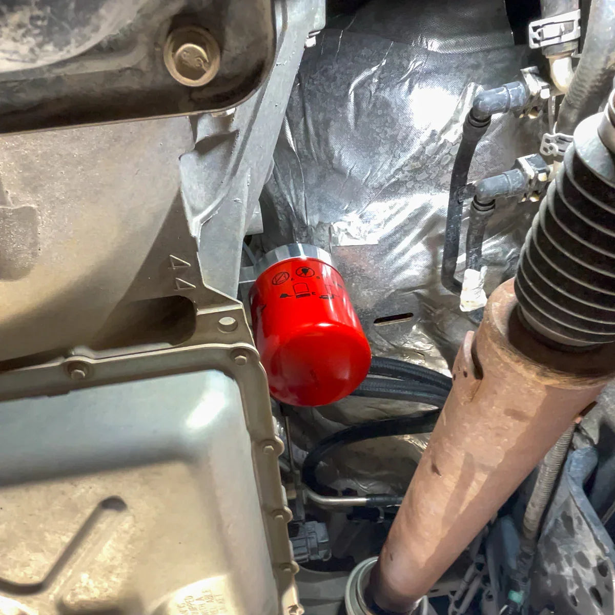 Installed Baldwin fuel filter mounted to H&S Motorsports relocation bracket under 2017–2023 Ford 6.7L Power Stroke, shown next to driveshaft and transmission pan.