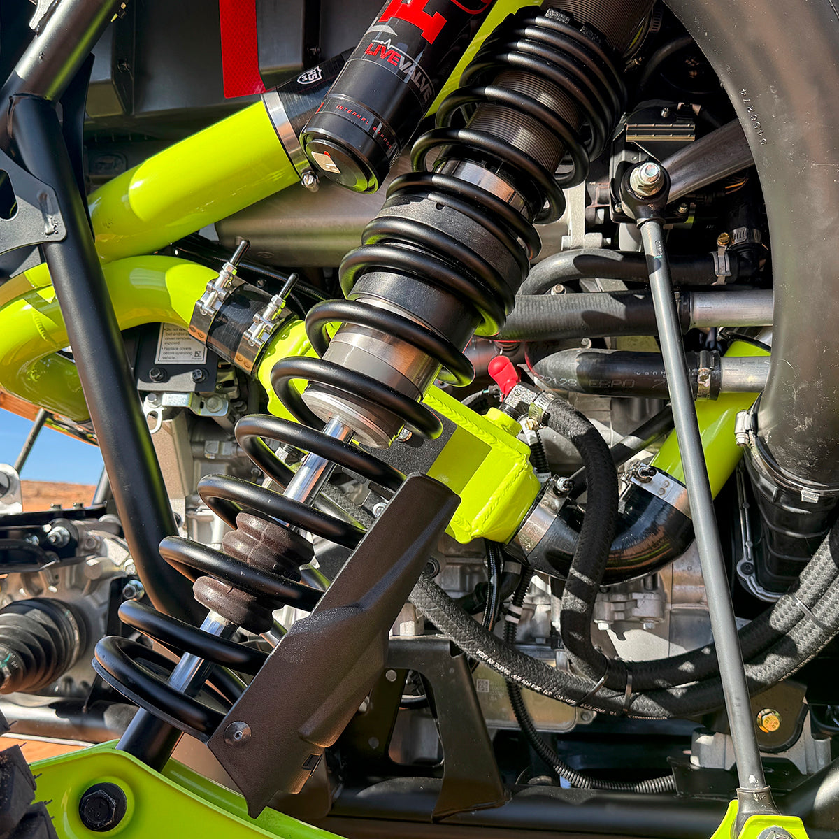 
                  
                    Close-up of the rear suspension and turbo piping on a Polaris RZR Pro R, showing upgraded charge pipes, FOX Live Valve shock, and performance hose routing.
                  
                