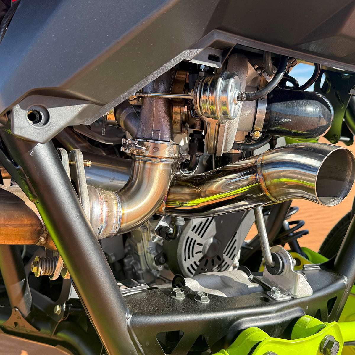 
                  
                    Close-up of the H&S Motorsports Easy-Boost Turbo Kit installed on a Polaris RZR Pro R, highlighting the polished stainless steel exhaust piping and mounted turbocharger within the engine bay.
                  
                